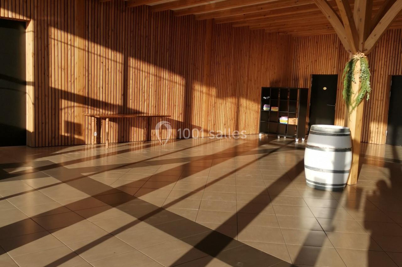 Salle lumineuse avec murs en bois, sol carrelé, tonneau blanc et ombres projetées par la lumière du soleil.