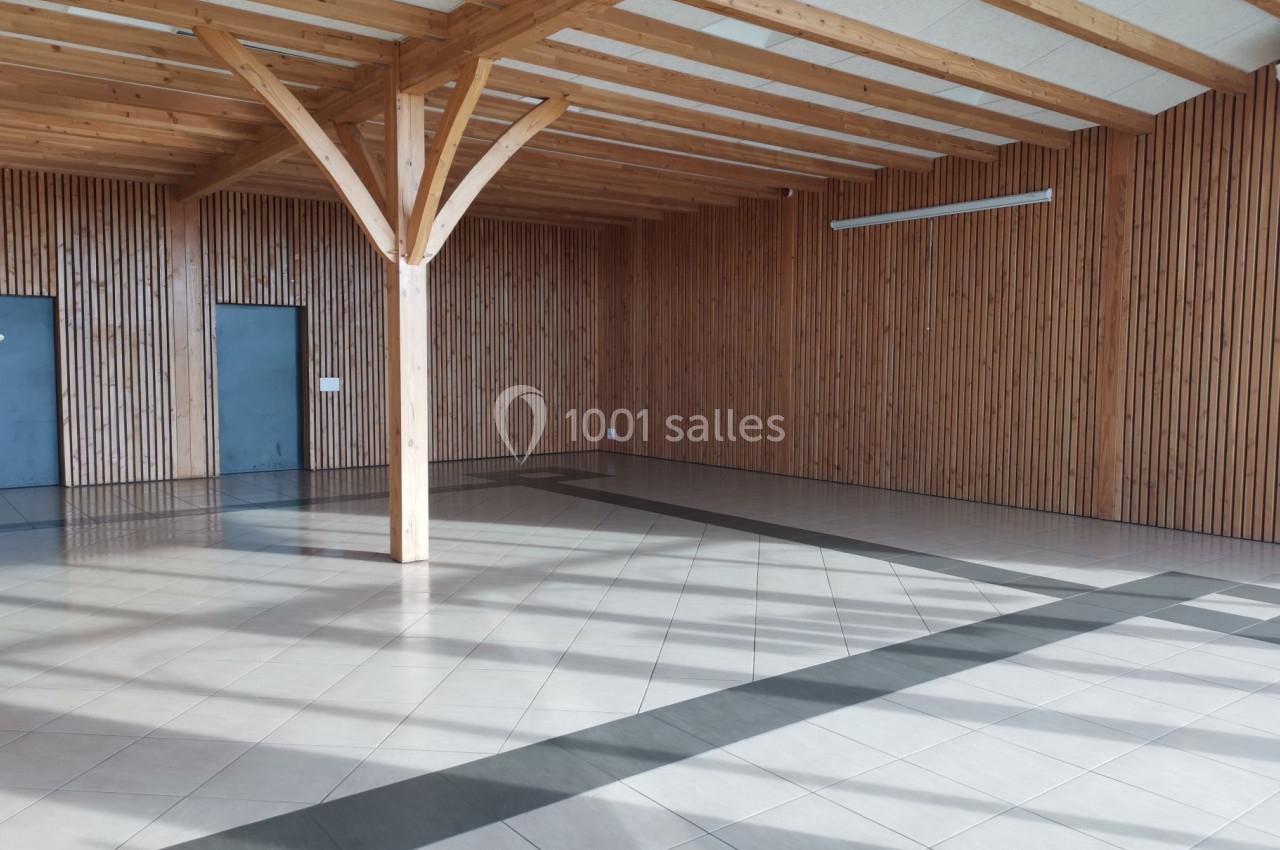 Salle vide avec murs en bois, sol carrelé clair et poutres apparentes sous un plafond incliné.