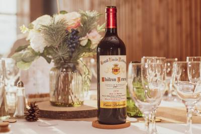 Champ de vignes baigné par la lumière dorée d'un coucher de soleil, avec des arbres et des bâtiments en arrière-plan.