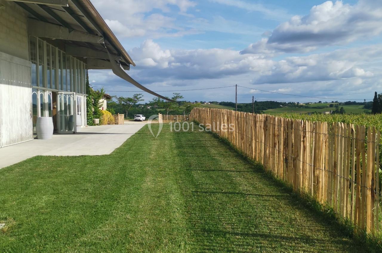 Pelouse bien entretenue longeant un bâtiment moderne avec une clôture en bois et un paysage rural en arrière-plan.