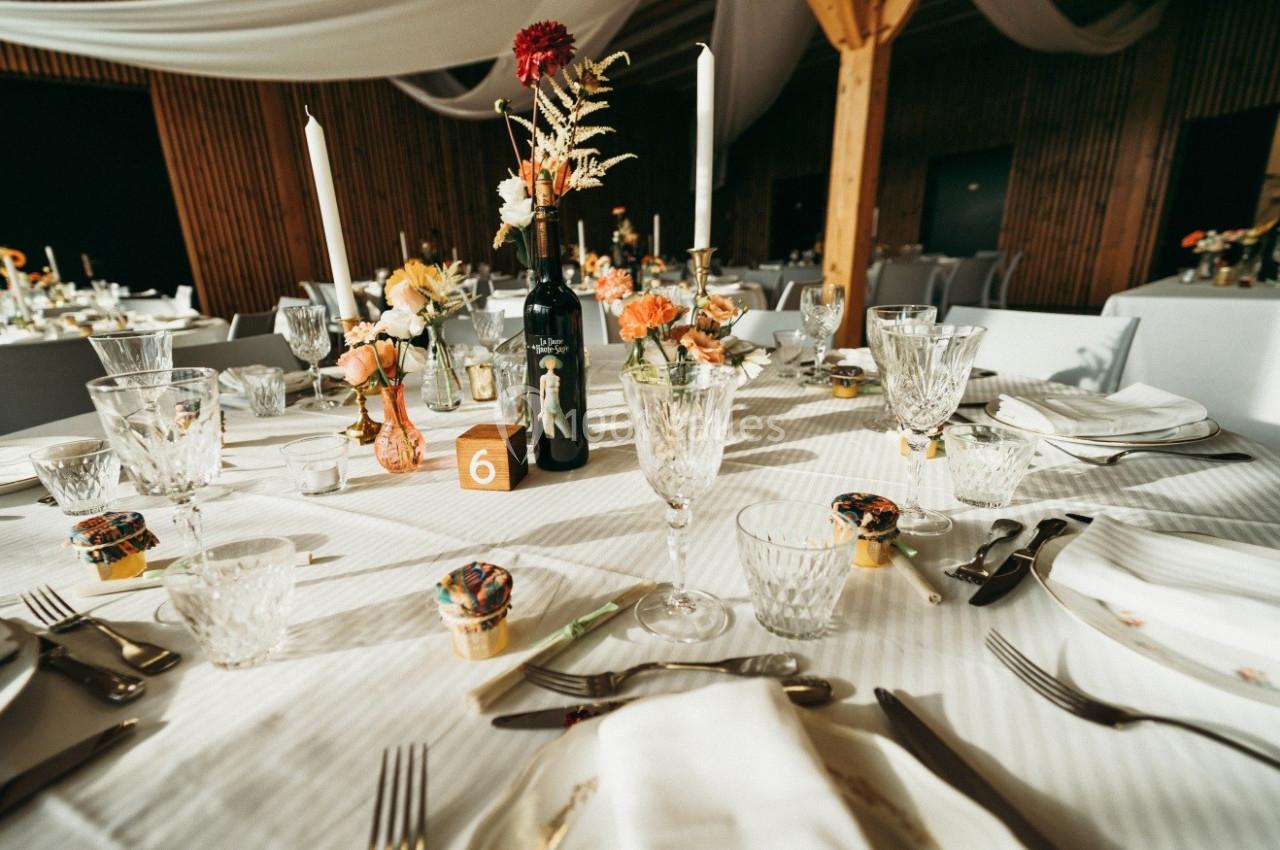 Table de réception décorée avec des fleurs, bougies, vaisselle élégante et une bouteille de vin au centre.