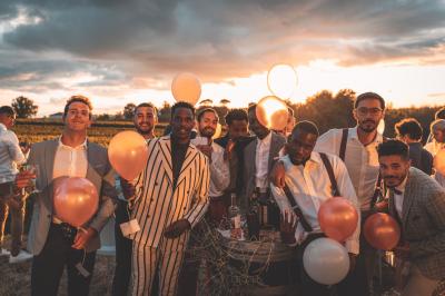 Champ de vignes baigné par la lumière dorée d'un coucher de soleil, avec des arbres et des bâtiments en arrière-plan.