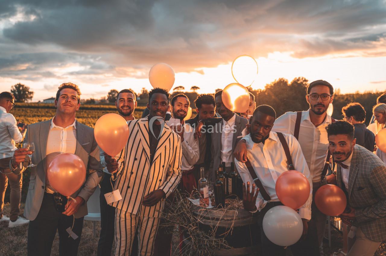 Un groupe d'hommes souriants tenant des ballons, rassemblés en extérieur au coucher du soleil.