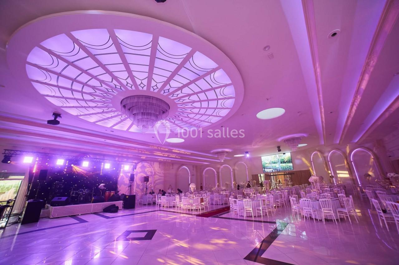 Salle de réception spacieuse avec plafond lumineux, tables rondes dressées et éclairage violet.
