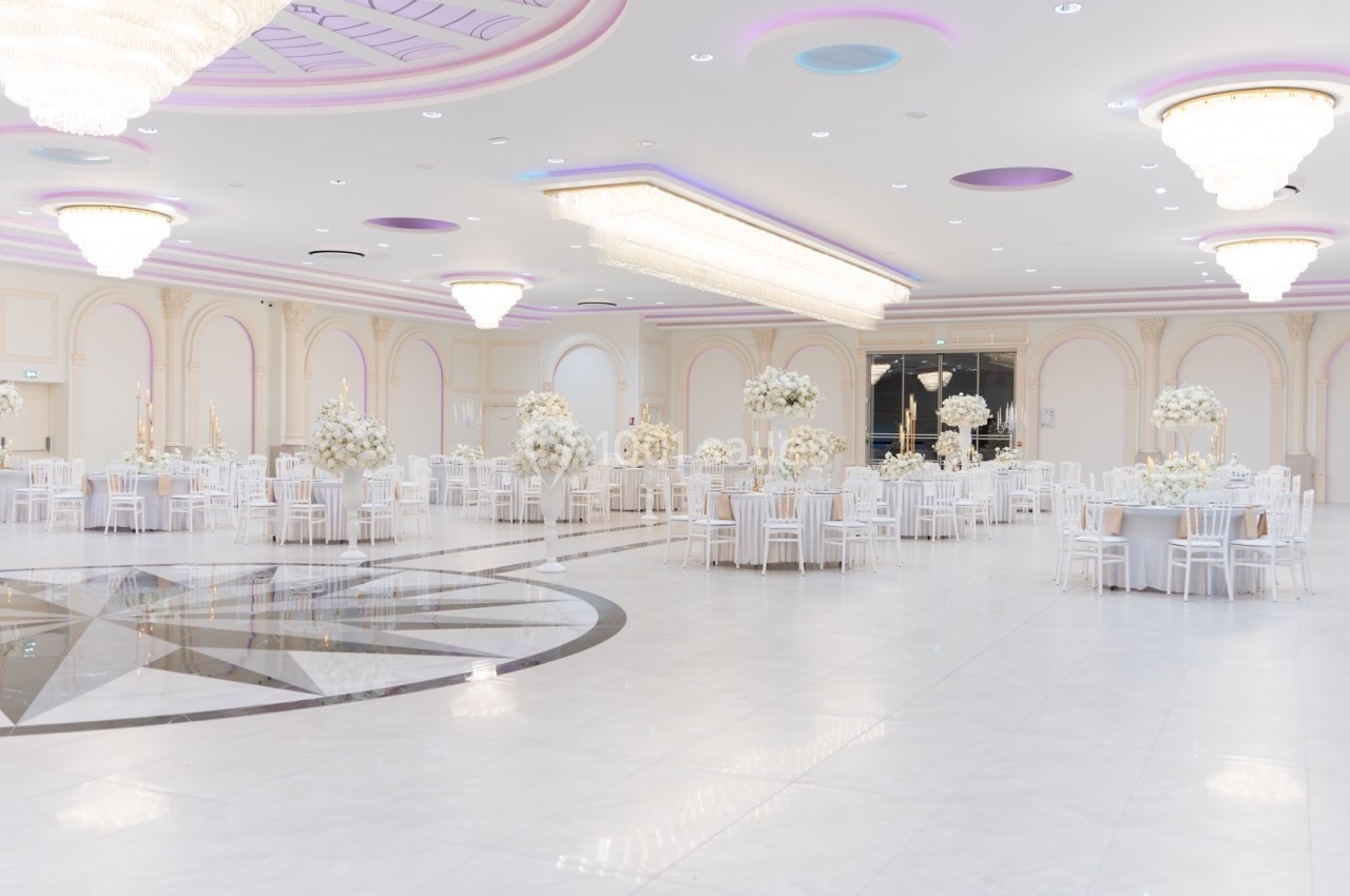 Salle de réception spacieuse et lumineuse, décorée de tables rondes blanches et de centres de table floraux élégants.