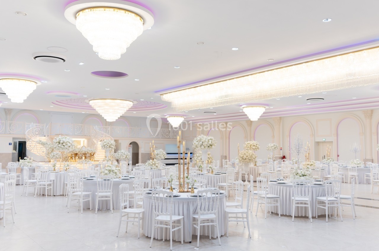 Salle de réception élégante avec tables rondes décorées de fleurs blanches et grands lustres suspendus.