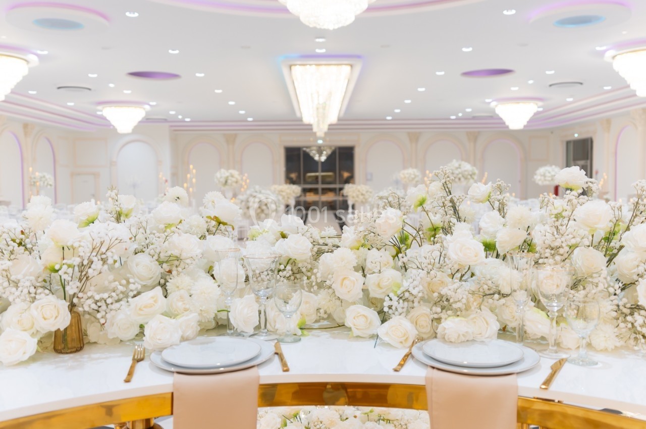 Salle de réception élégante avec une table décorée de fleurs blanches et un éclairage lumineux.