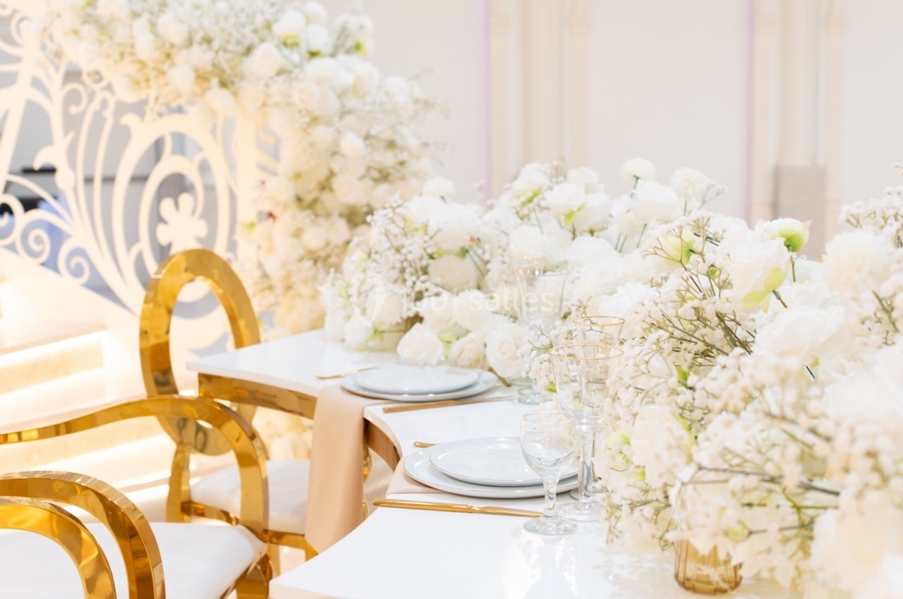 Table de réception élégamment décorée de fleurs blanches, avec des chaises dorées et une ambiance lumineuse.