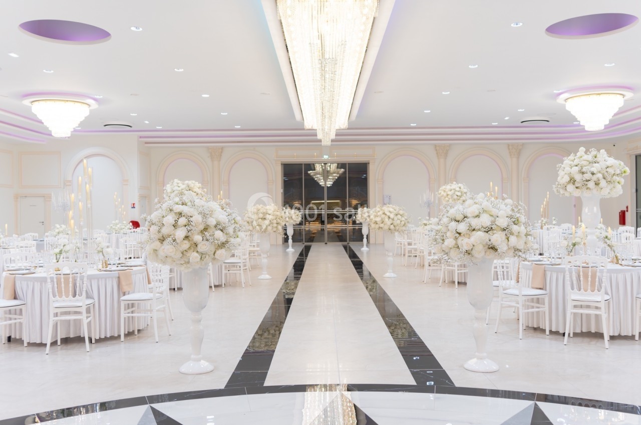Salle de réception élégante avec tables rondes décorées de fleurs blanches et grand lustre central lumineux.
