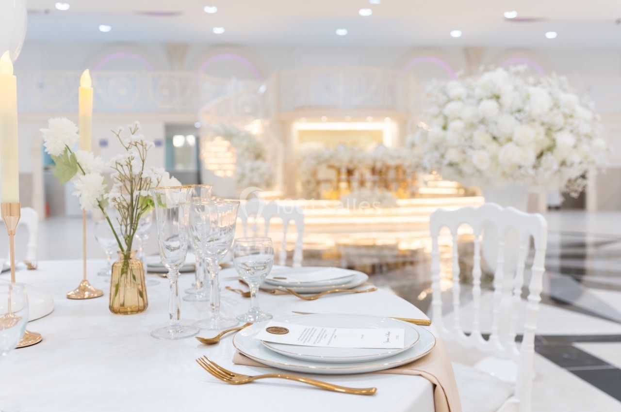 Table élégamment dressée avec vaisselle blanche, verres en cristal et décorations florales dans une salle de réception…
