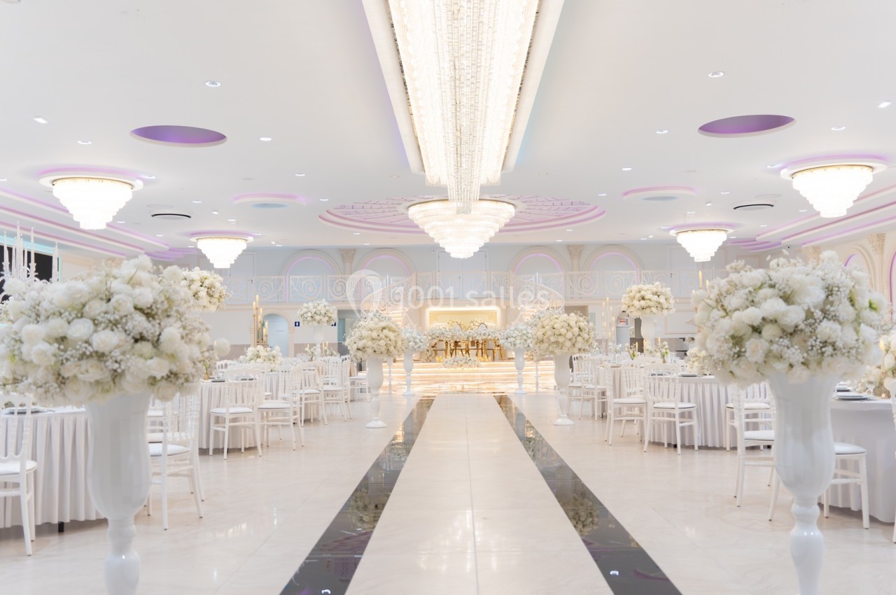 Salle de réception élégante avec tables dressées, décorations florales blanches et lustres imposants.