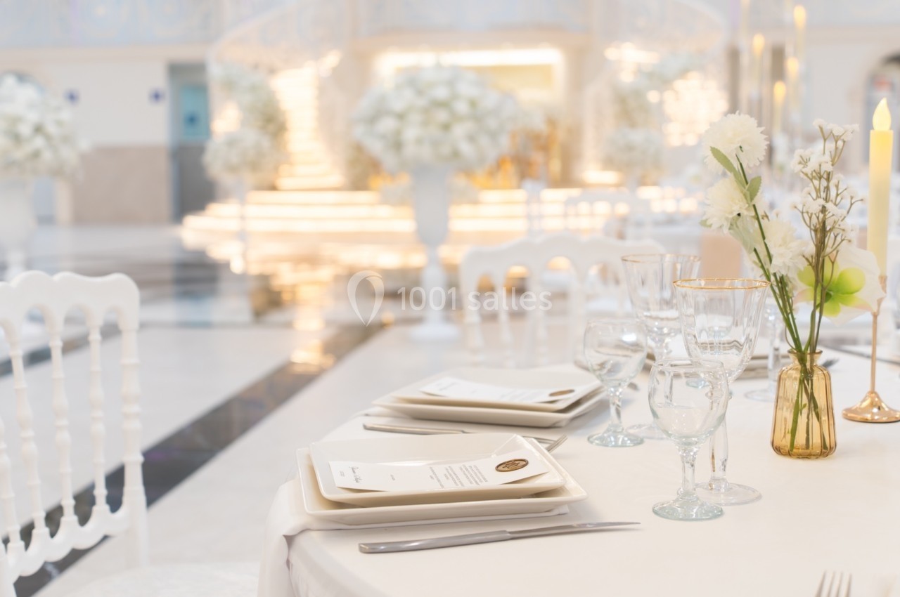 Table élégamment dressée avec vaisselle blanche, verres et décoration florale, dans une salle lumineuse et raffinée.