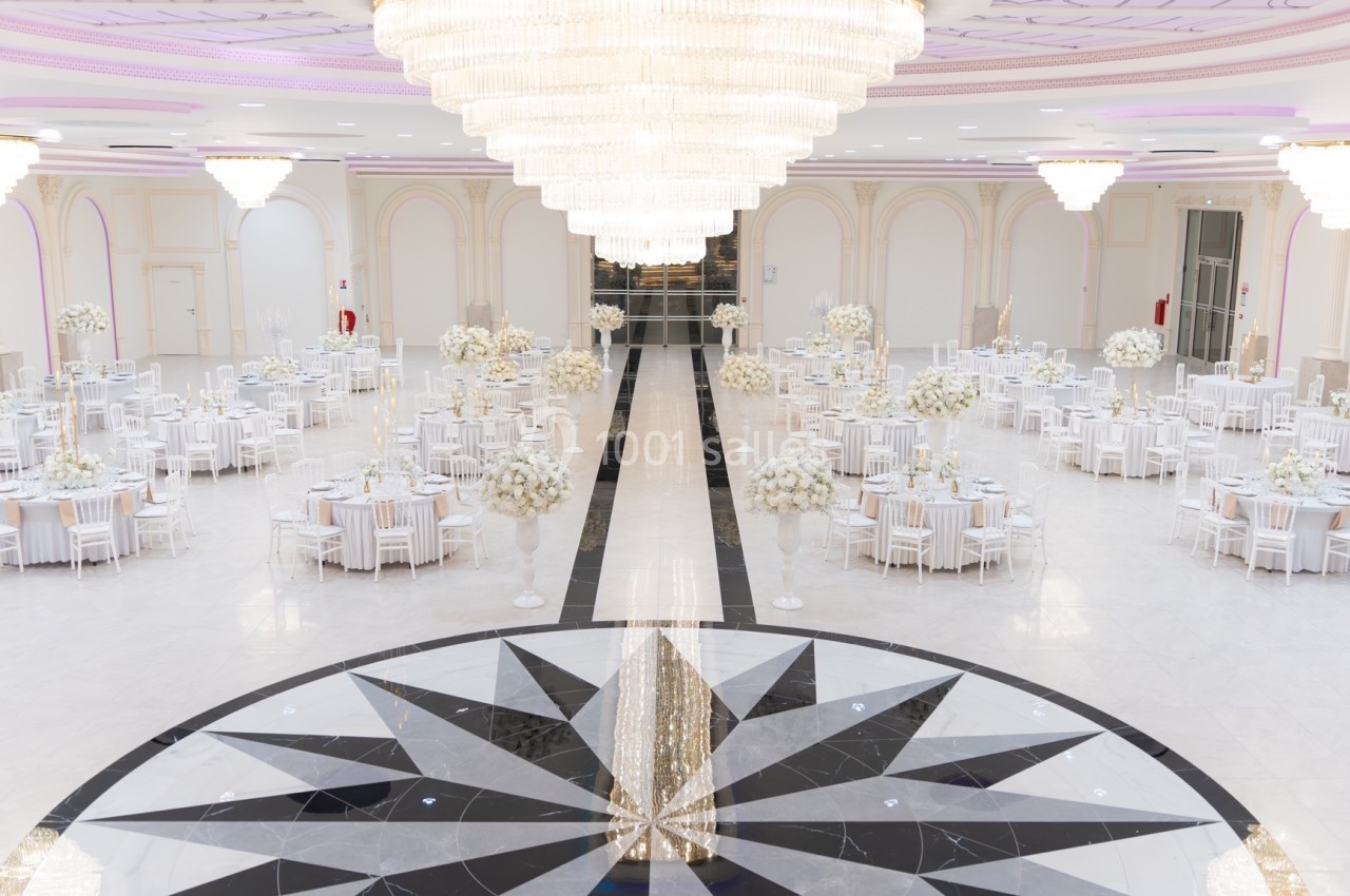 Salle de réception élégante avec tables rondes décorées de fleurs blanches et grand lustre central lumineux.