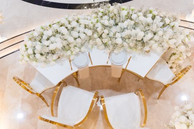 Vue aérienne d'une table élégante décorée de fleurs blanches avec des chaises dorées et un sol en marbre clair.