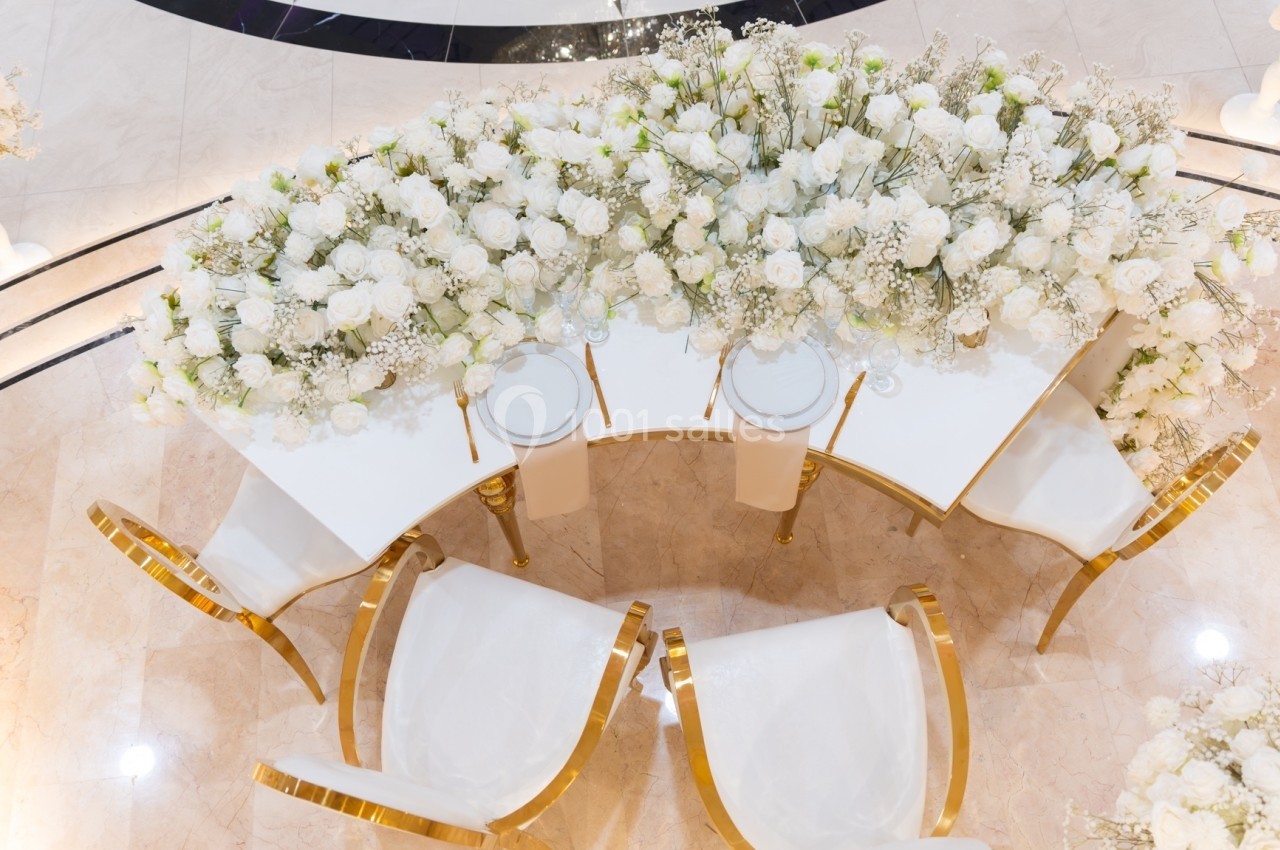 Vue aérienne d'une table élégante décorée de fleurs blanches avec des chaises dorées et un sol en marbre clair.
