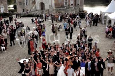 Salle en pierre avec poutres apparentes, tables rondes dressées et décorations lumineuses pour un événement.