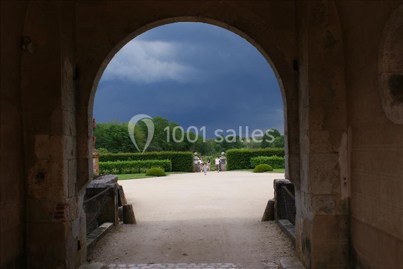 Vue d'un jardin verdoyant sous un ciel orageux, encadrée par une arche en pierre.
