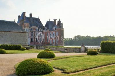 Vue aérienne d'un château entouré d'un parc, d'un étang et d'un village avec des maisons et des espaces verts.