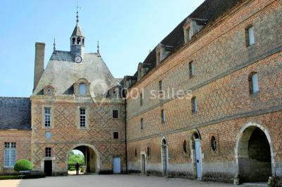 Vue aérienne d'un château entouré d'un parc, d'un étang et d'un village avec des maisons et des espaces verts.