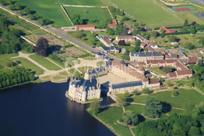 Vue aérienne d'un château entouré d'un parc, d'un étang et d'un village avec des maisons et des espaces verts.