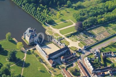 Vue aérienne d'un château entouré d'un parc, d'un étang et d'un village avec des maisons et des espaces verts.