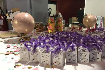 Globes décoratifs, confettis colorés et petites boîtes blanches ornées de rubans violets disposés sur une table festive.