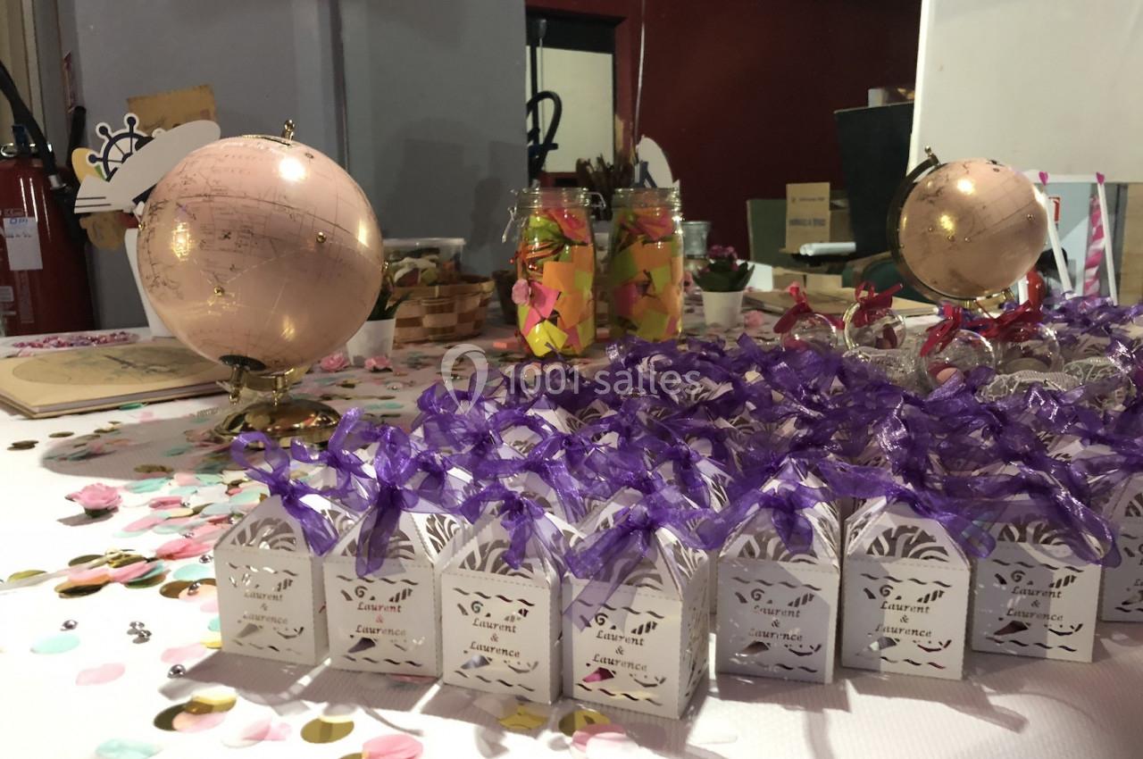 Globes décoratifs, confettis colorés et petites boîtes blanches ornées de rubans violets disposés sur une table festive.