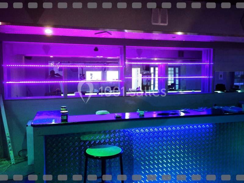 Comptoir de bar avec tabouret, éclairé par des néons violets et bleus, dans un espace intérieur moderne.