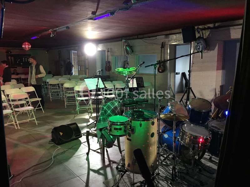 Salle de répétition avec instruments de musique, dont une batterie et des percussions, et des chaises disposées en arrière…