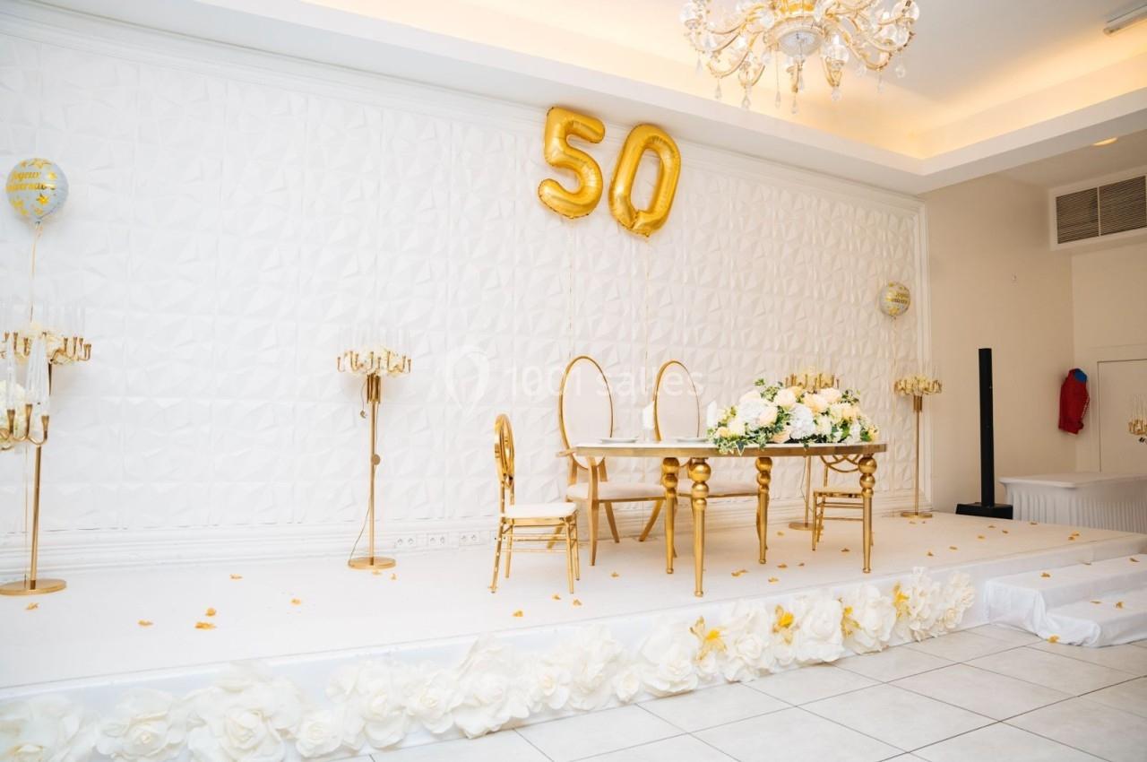 Salle décorée pour une célébration avec une table ornée de fleurs blanches et des ballons dorés formant le chiffre 50.