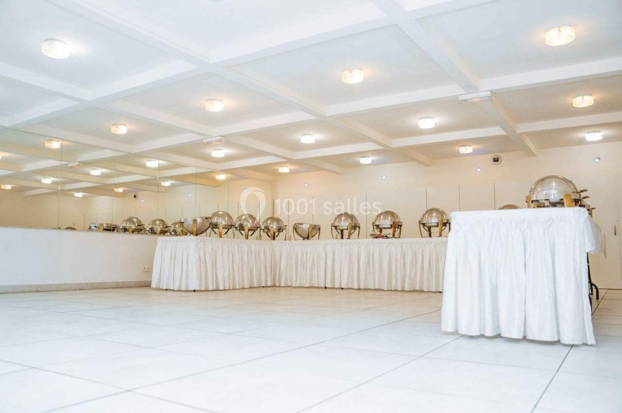 Salle lumineuse avec un buffet de plats sous cloches argentées, disposé sur des tables recouvertes de nappes blanches.