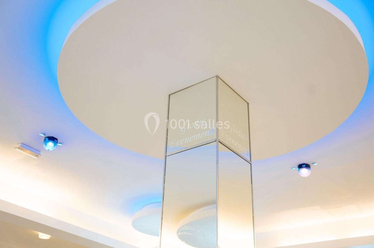 Plafond lumineux avec éclairage bleu et blanc, reflété par une colonne en miroir au centre.