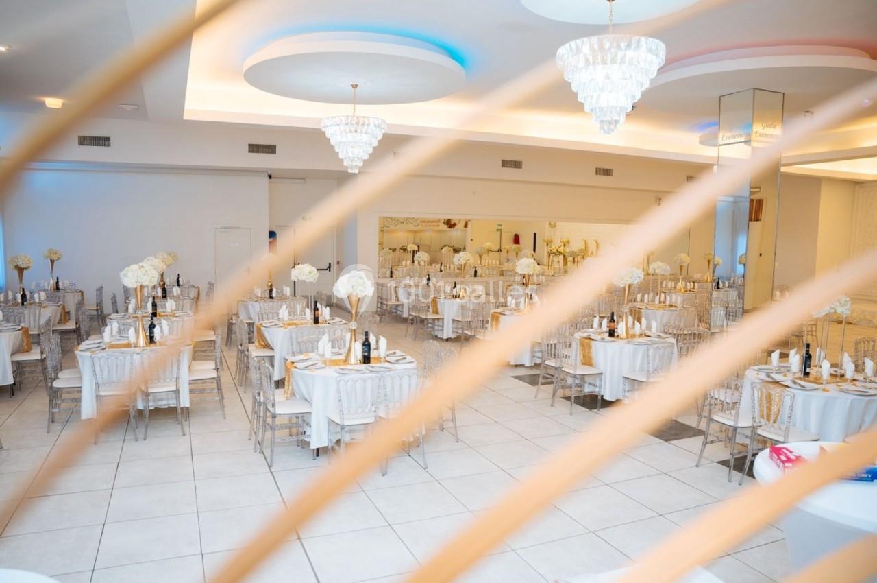 Salle de réception élégante avec tables dressées, décorations florales blanches et lustres suspendus.