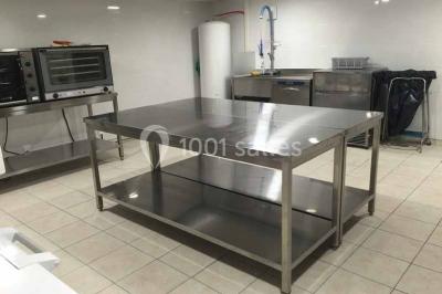 Table en inox avec étagère inférieure dans une cuisine professionnelle équipée de fours et d'équipements.