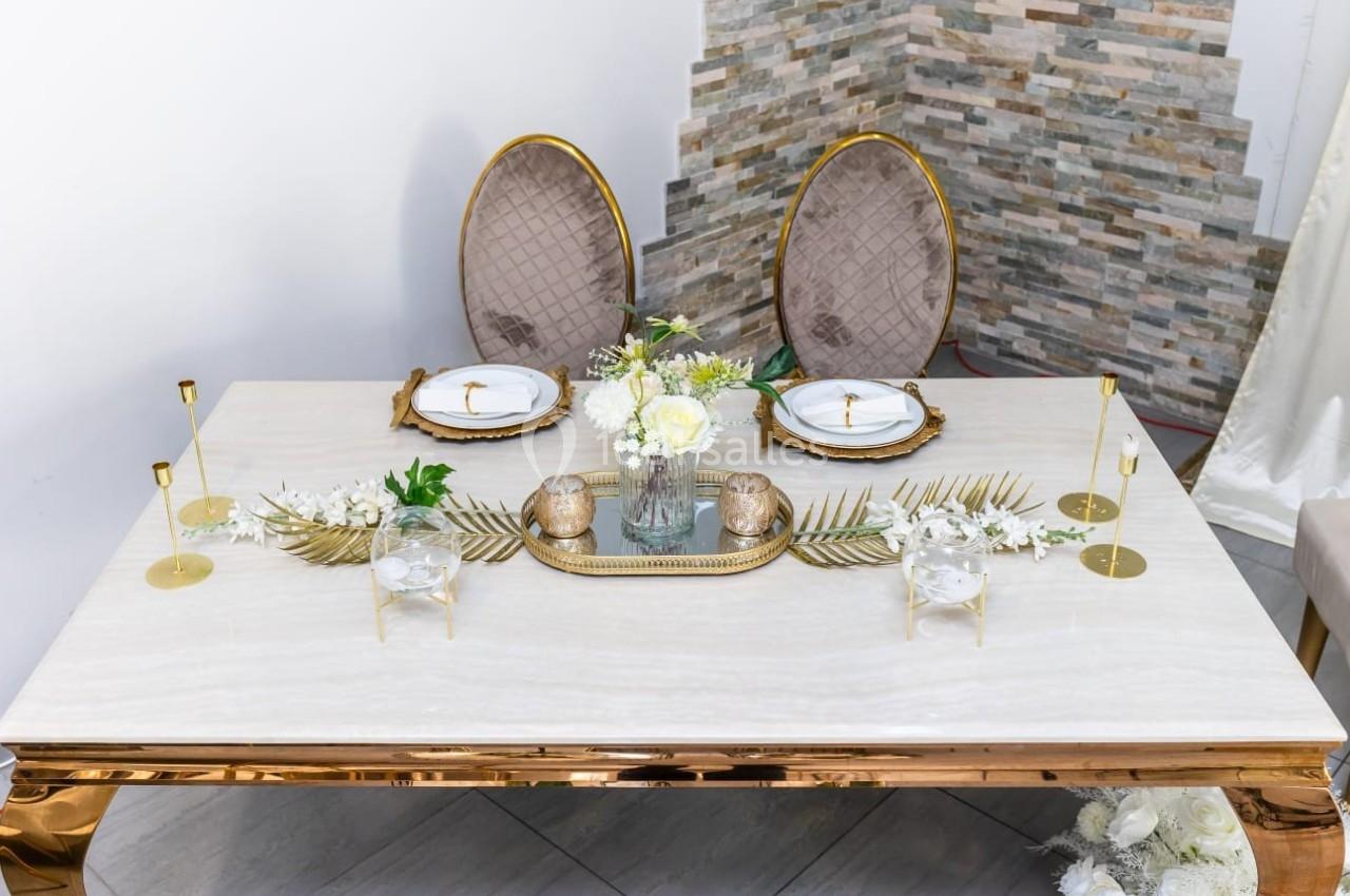 Table élégante décorée avec des assiettes blanches, des bougies dorées et un centre de table floral sur fond de mur en…