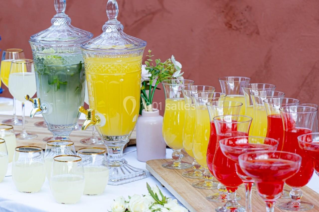 Deux distributeurs de boissons et des verres remplis de jus colorés disposés sur une table blanche.