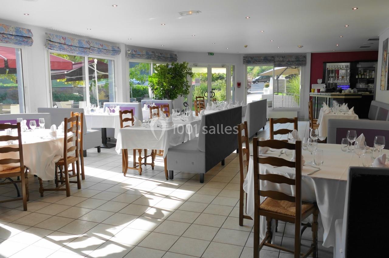 Salle de restaurant lumineuse avec des tables dressées, des chaises en bois et de grandes baies vitrées donnant sur l…
