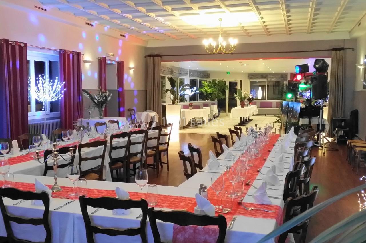 Salle de réception décorée avec des tables dressées, nappes blanches, chemins de table rouges et éclairages festifs.