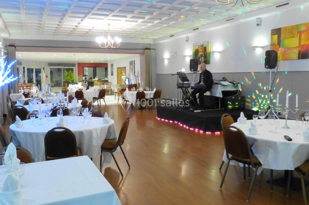 Salle de réception lumineuse avec tables dressées, un musicien jouant sur scène et des décorations modernes.