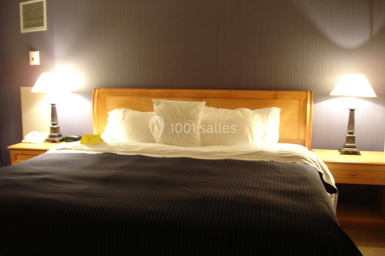 Lit double avec tête de lit en bois, couvertures sombres et deux lampes allumées sur des tables de chevet.