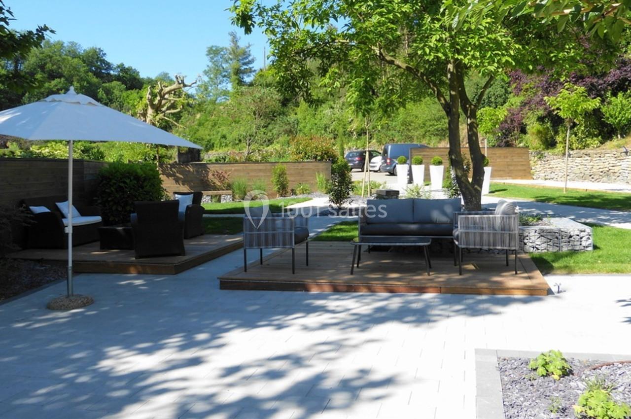 Terrasse extérieure avec mobilier de jardin, parasol blanc et espaces verts arborés en arrière-plan.