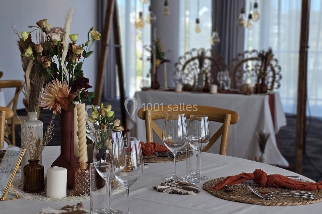 Table décorée avec des fleurs séchées, bougies et vaisselle élégante dans une salle lumineuse avec des tables en arrière…