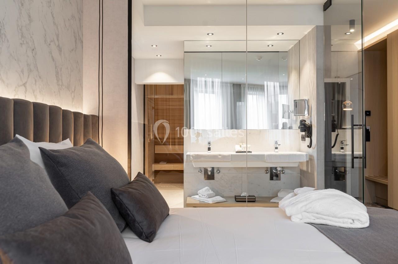 Chambre d'hôtel moderne avec lit double, salle de bain vitrée, lavabo double et lumière naturelle.