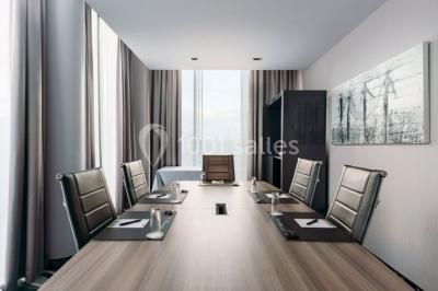 Salle de réunion moderne avec table rectangulaire, chaises noires, écran mural, tableau blanc et minibar.