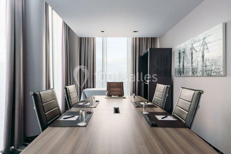 Salle de réunion moderne avec table en bois, chaises en cuir noir, blocs-notes, stylos et grandes fenêtres.