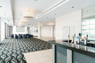 Salle de réunion moderne avec table rectangulaire, chaises noires, écran mural, tableau blanc et minibar.