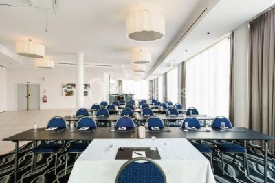 Salle de réunion moderne avec table rectangulaire, chaises noires, écran mural, tableau blanc et minibar.