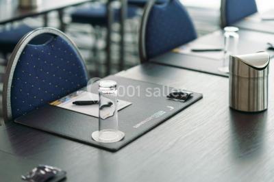 Salle de réunion moderne avec table rectangulaire, chaises noires, écran mural, tableau blanc et minibar.