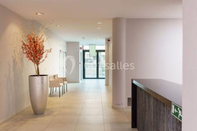 Salle de réunion moderne avec table rectangulaire, chaises noires, écran mural, tableau blanc et minibar.