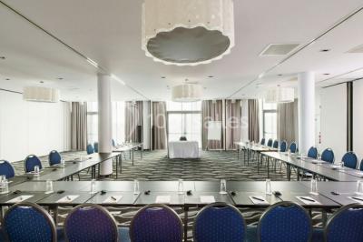 Salle de réunion moderne avec table rectangulaire, chaises noires, écran mural, tableau blanc et minibar.